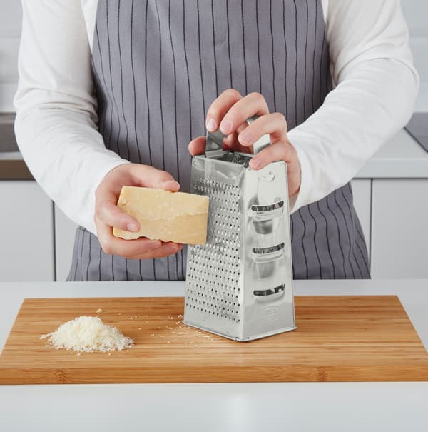 Iemand raspt een stuk kaas met een staande rasp.