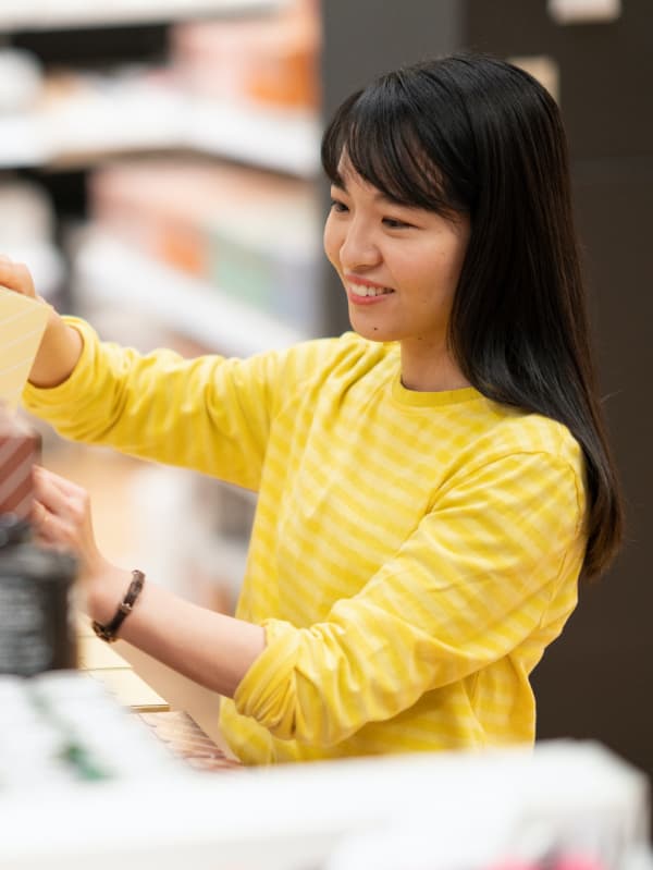 イエローのボーダーシャツを着たコワーカーが、イケアストアの売場でカラーカードを手に取り、ホームファニッシングのデコレーションを確認している。
