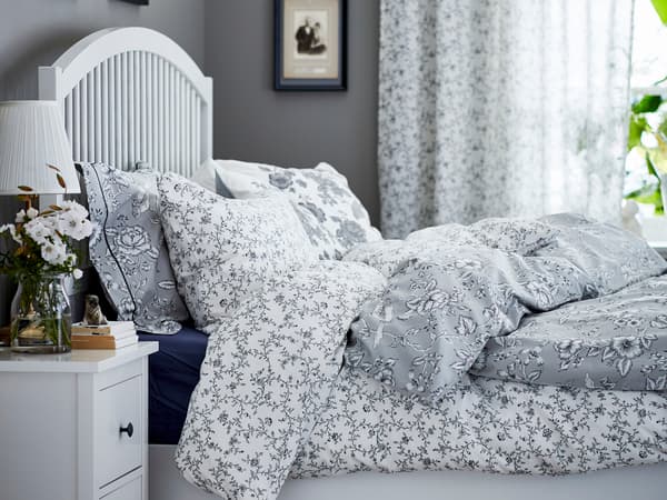 白いヘッドボードのベッドにグレーの花柄寝具を合わせたクラシックな寝室。カーテンで柔らかな印象。