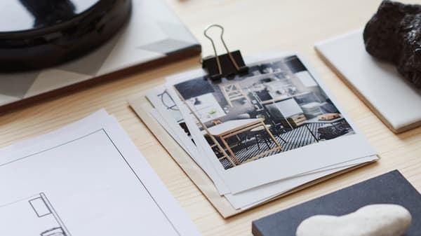 원목 테이블에 IKEA 인테리어 디자인 사진 여러 장이 집게로 묶여 있고, 그 옆으로 스케치한 도안의 모서리가 보입니다.