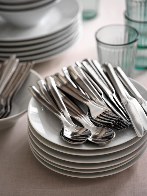 ערמת צלחות, כוסות וסכו"ם מקולקציית IKEA 365+‎ מונחים על משטח עליון לשולחן עם מפה ורודה.