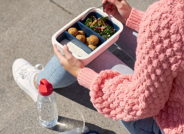 IKEA 플라스틱 식품보관용기에 담긴 도시락을 먹고 있는 한 여성과 그 옆에 놓인 투명 플라스틱 물병