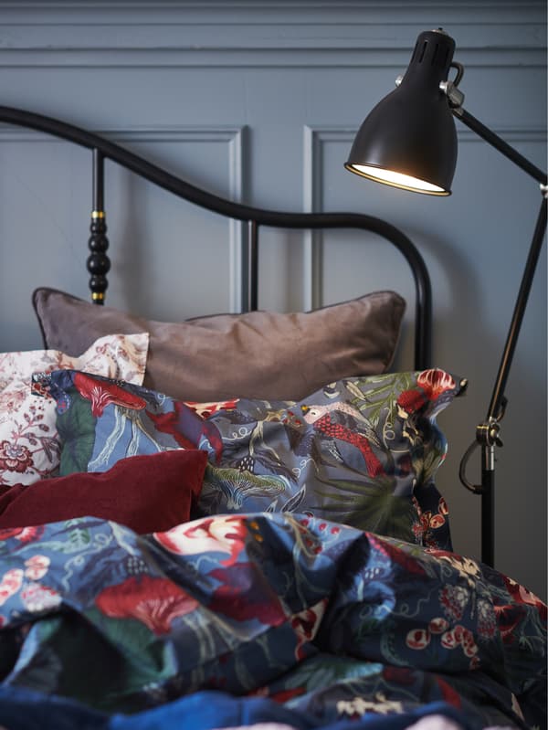 IKEA ARÖD floor lamp in dark grey anthracite next to a bed with colourful floral bedding.