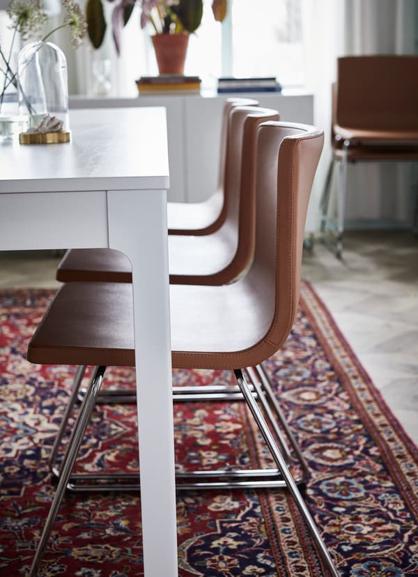 IKEA BERNHARD stoelen in goudbruin leder staan op een rij aan een witte eettafel.