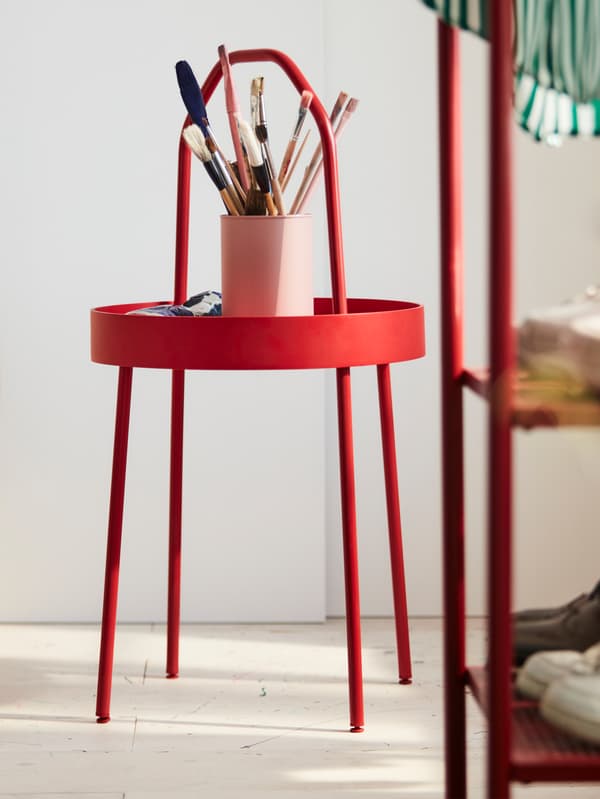 IKEA BURVIK side table in red with a cup filled of paint brushes in a room with white walls and floors.