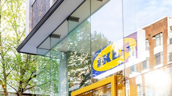 IKEA byggnad med glasfasad som speglar träd och byggnader, IKEA loggan synlig på glaset. 