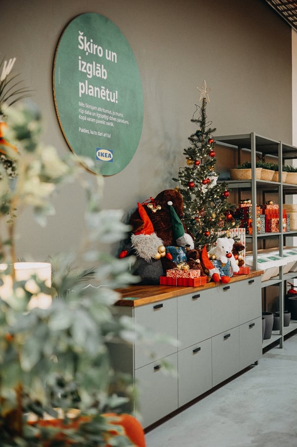 IKEA Christmas corner with decorated tree, plush toys, wrapped gifts, and green “Save the Planet” wall sign.