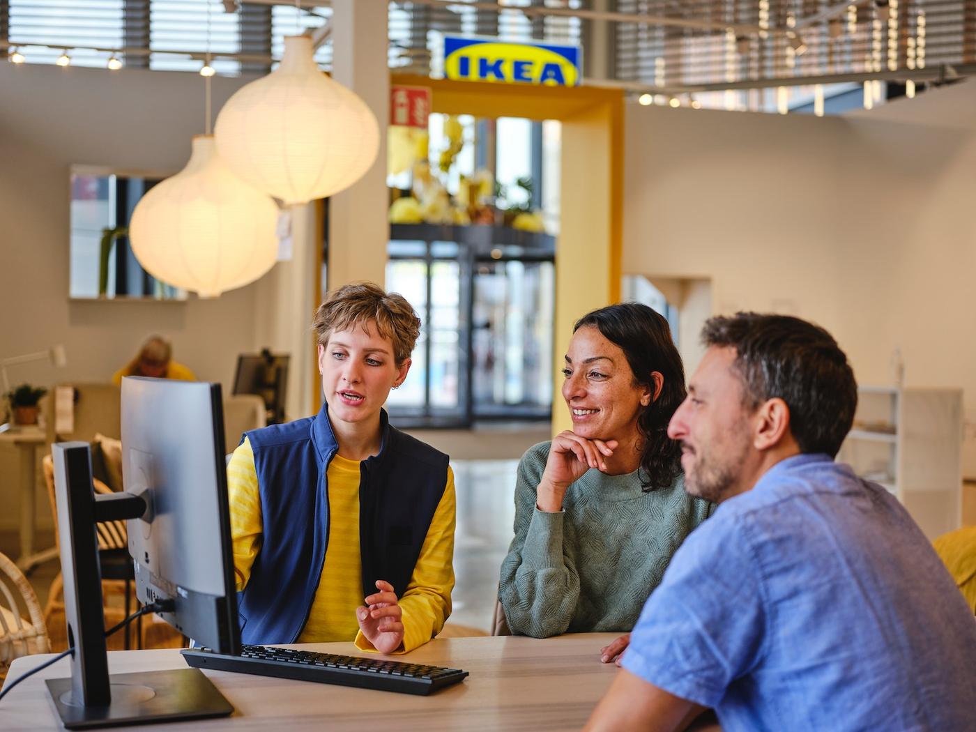 IKEA co-worker advises two customers at a computer in a bright furniture showroom.