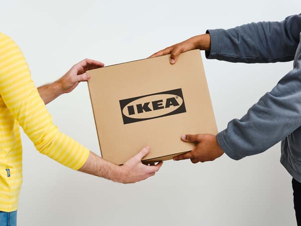 IKEA co-worker dressed in yellow handing over a cardboard box with IKEA logo to a customer.