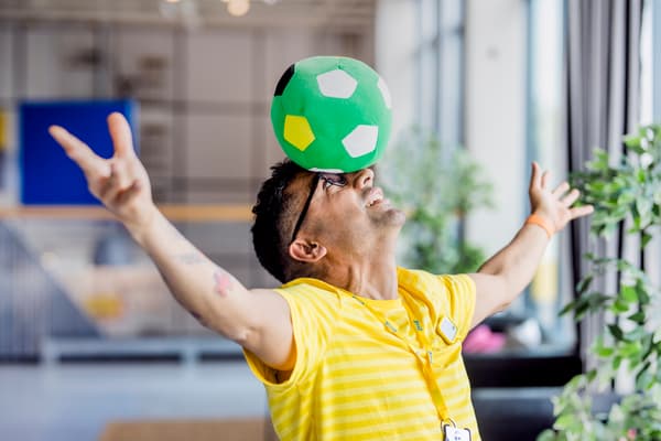 IKEA co-worker in a yellow shirt balancing a green football on their head.