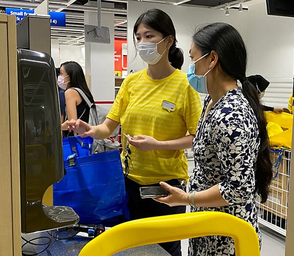 IKEA co-worker in uniform assisting a customer at checkout instore
