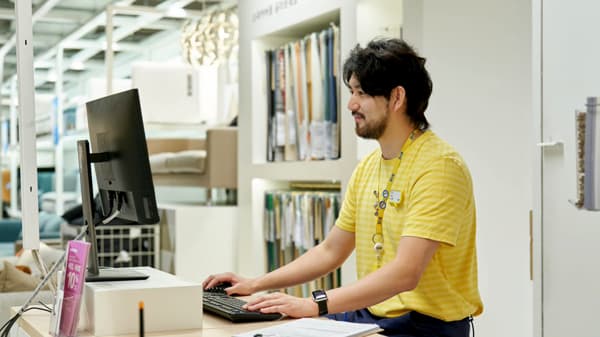 IKEA co-worker in yellow uniform working at a service counter computer in the store.