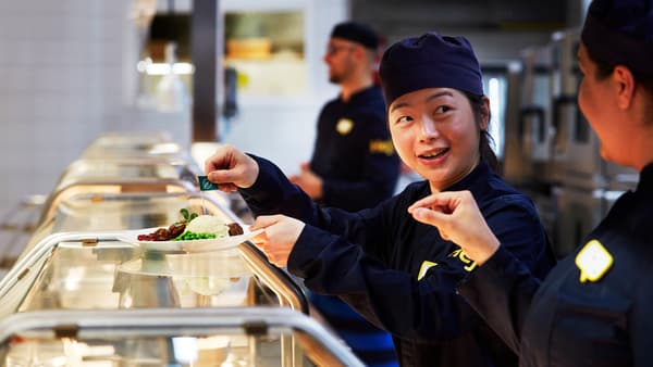 IKEA co-workers wearing dark blue uniforms plating up meals in the restaurant.