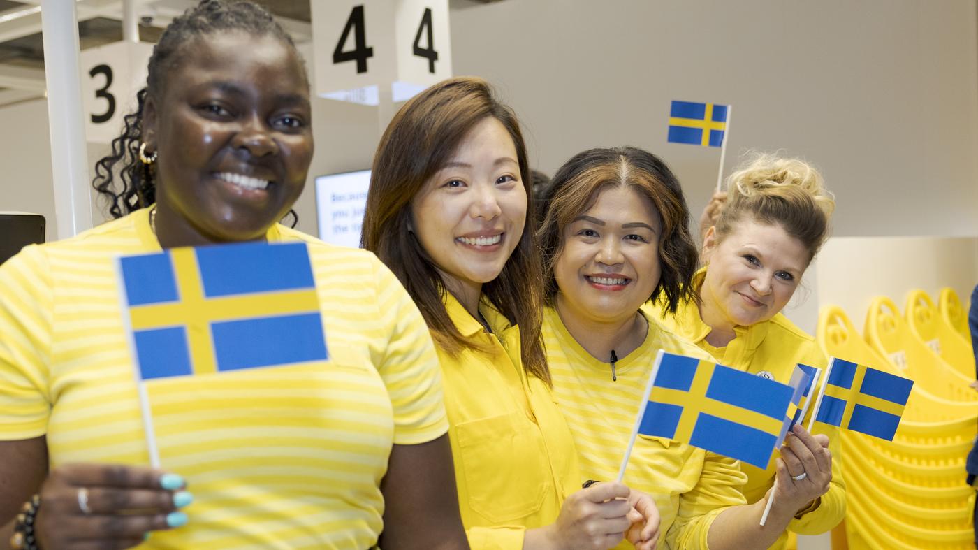 IKEA co-workers wearing yellow uniforms wave Swedish flags and smile at the camera.