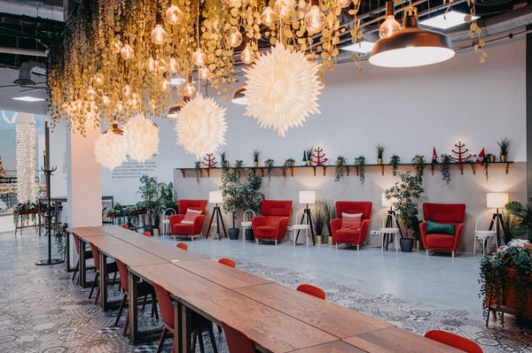 IKEA co-working space with long wooden tables, red chairs, hanging greenery, and bright pendant lighting.