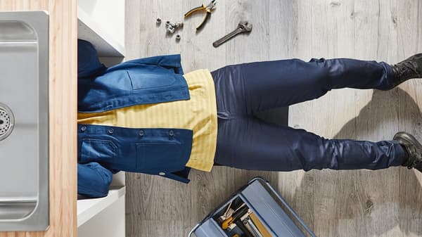 IKEA customer service employee in yellow shirt and blue work jacket professionally repairs a kitchen sink.