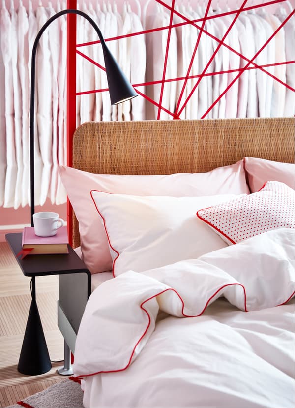 IKEA DELAKTIG bedframe with add-on rattan headboard and black standing lamp with side table.