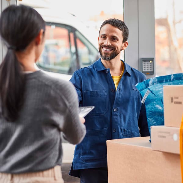 IKEA delivery man standing at the front door to a home handing cardboard boxes to a woman