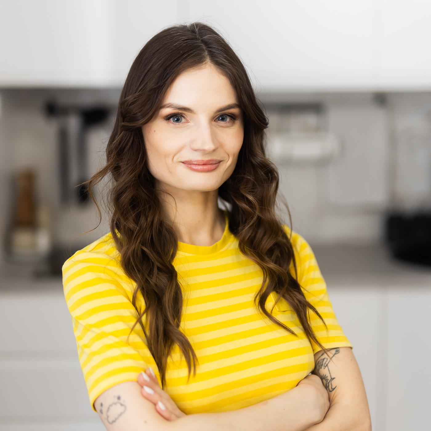 IKEA dizainere dzeltenā formas tērpā stāv virtuvē un smaida.