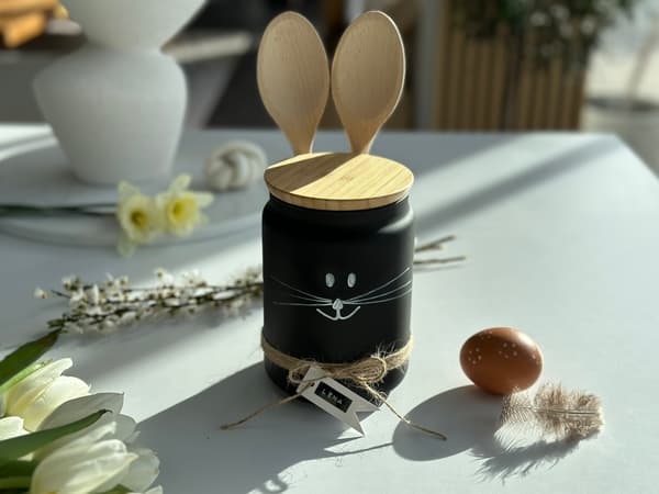 IKEA Eklatera Dose mit zwei MIXA Kochlöffel zu einem Hasen gestaltet. DIe Dose steht auf einem Tisch, der für Ostern geschmückt ist. 