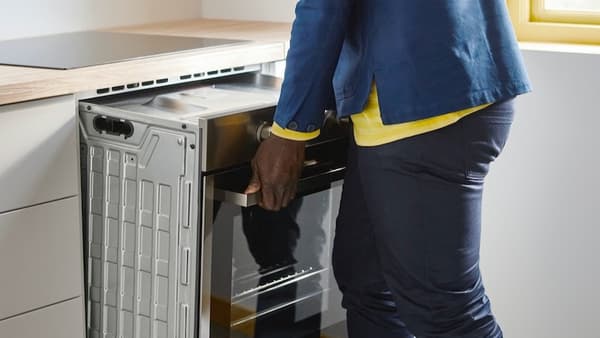 IKEA employee installs a modern built-in oven in a new IKEA kitchen with a light wooden countertop. Professional installation service and high-quality IKEA kitchen appliances in action.