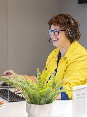 Ikea employee smiles talking on the phone with a customer. She is working on her laptop to support him with his request