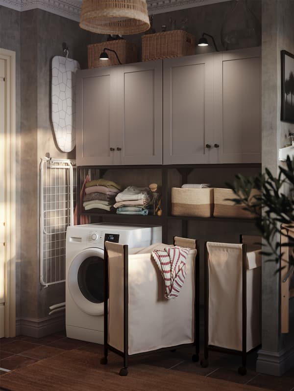 IKEA ENHET storage combination with baskets on shelves in a laundry room, a washing machine and two laundry bags on castors.