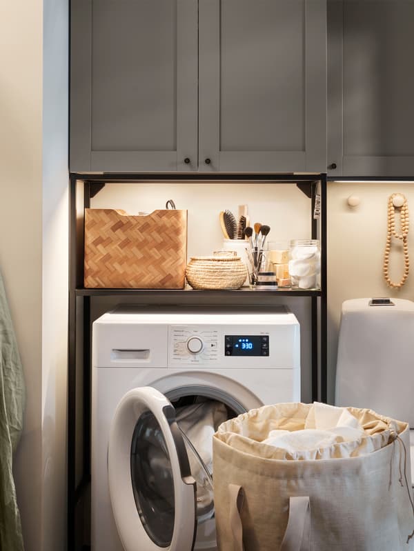 IKEA ENHET storage combination with grey fronts is standing in a small bathroom that has an UDDARP washer/dryer combination.