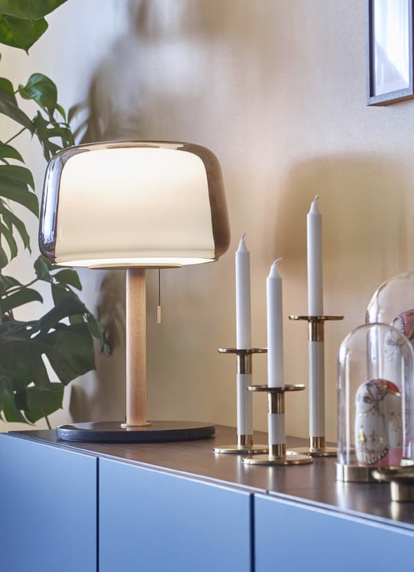 IKEA EVEDAL modern dome-shaped table lamp next to three GLITTRIG white and gold coloured candle sticks and BEGÅVNING glass domes.