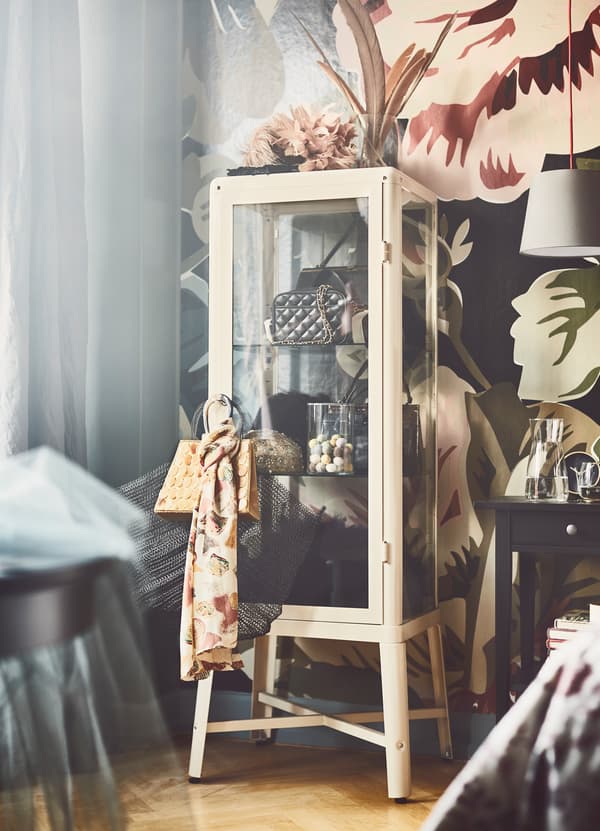 IKEA FABRIKÖR glass door cabinet with an off-white cream framed coating storing purses and accessories.