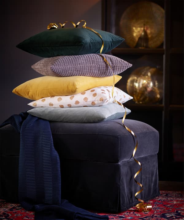 IKEA FÄRLÖV foot stool on a red patterned rug, stacked high with pillows in assorted colours.