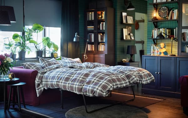 IKEA GRÖNLID red sofa made out into a sofa bed with brown and white checkered bedsheets.