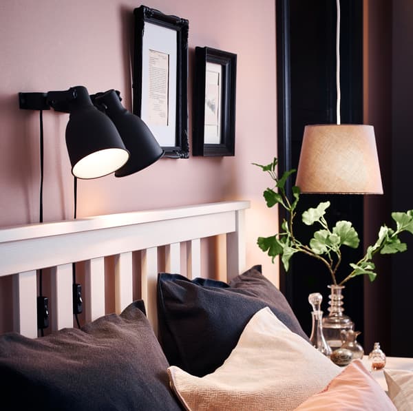 IKEA HEKTAR black mounted lamplights above a white HEMNES bedframe, turned on to emit a warm glow.