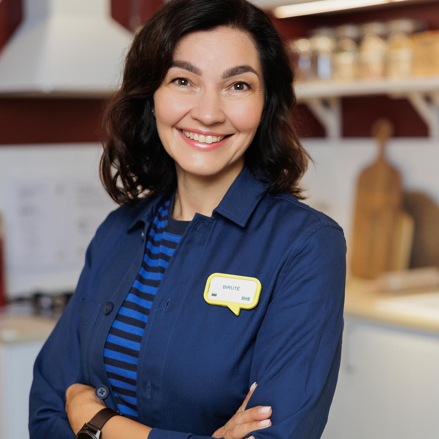 IKEA interior designer in a blue uniform, smiling confidently in a modern kitchen showroom.