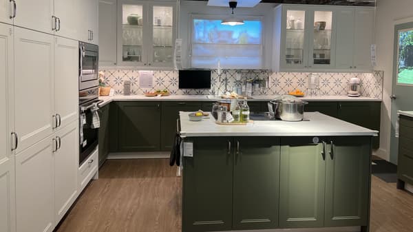IKEA kitchen with green lower cabinets and white upper cabinets. There is an island, sink, and oven in the photo as well. 