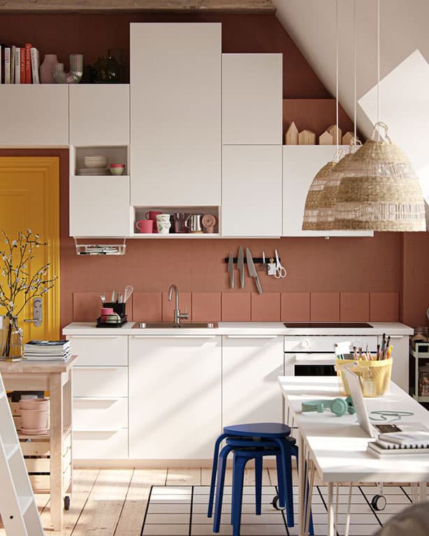 IKEA Küchenlosung mit weißen Unter - und Oberschränken. Zu sehen ist auch ein kleinerere Esstisch mit blauen hockern und 2 Hängelampen über dem Tisch