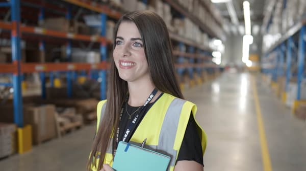 „IKEA Lager-Mitarbeiterin mit Sicherheitsweste und Klemmbrett im modernen Hochregallager – Fokus auf Organisation und effiziente Logistik bei IKEA.