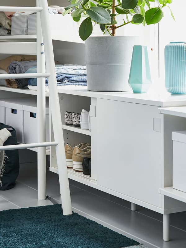 IKEA MACKAPÄR white bench, next to a ladder, revealing four pairs of shoes being stored in the storage unit.