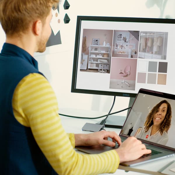 IKEA medarbetare står vid ett skrivbord med laptop och skärm, tittar på inredningsidéer och har videosamtal.