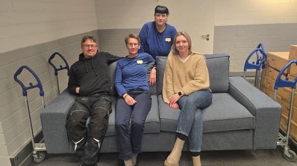 IKEA Mitarbeitende und Mitarbeitende der Jugendhilfe Grünau Bielefeld sitzen auf einem Sofa. Daneben ist ein Einkaufswagen mit Paketen zu sehen. 