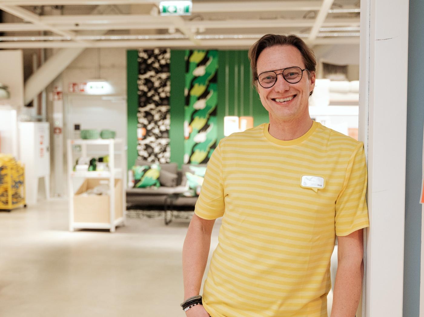 Ikea Mitarbeiter im gelbem T-Shirt steht vor einem Ikea Showroom