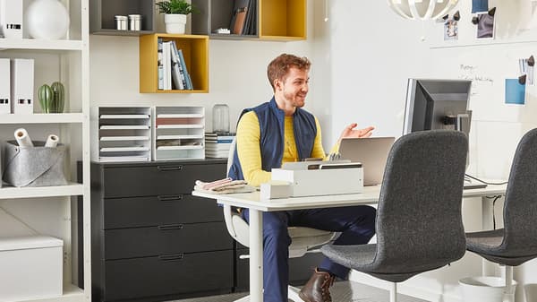 Ikea Mitarbeiter sitzt an einem Schreibtisch in einem modern eingerichteten Homeoffice mit Regalen, Stauraum und Computerarbeitsplatz