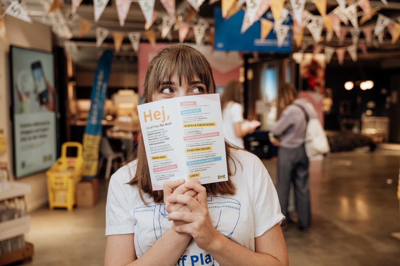 IKEA Mitarbeiterin hält das Programm des IKEA Festivals vor ihr Gesicht.