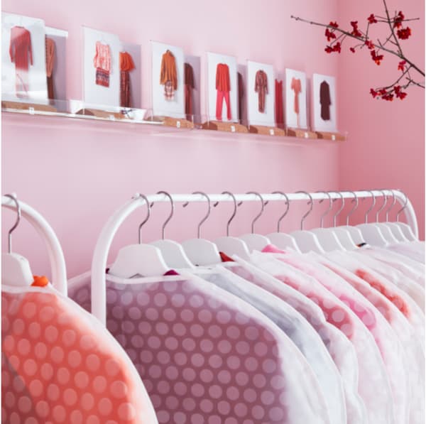 IKEA MULIG white clothes rack with clothes in protective transparent covers.