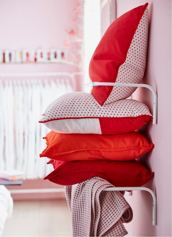IKEA MULIG white clothes rail with cushions and textiles stacked in between.