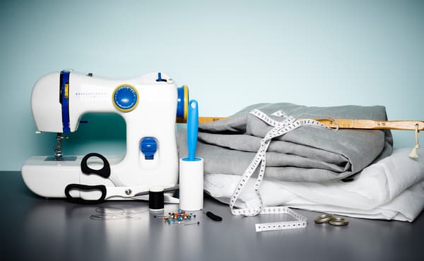 IKEA naaimachine, stof, meetlint, spelden, schaar en katoendraad op een tafel naast de wand