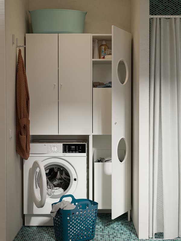 IKEA NYSJÖN white cabinets next to a shower, a white washing machine and a green basket on a green-tiled floor.