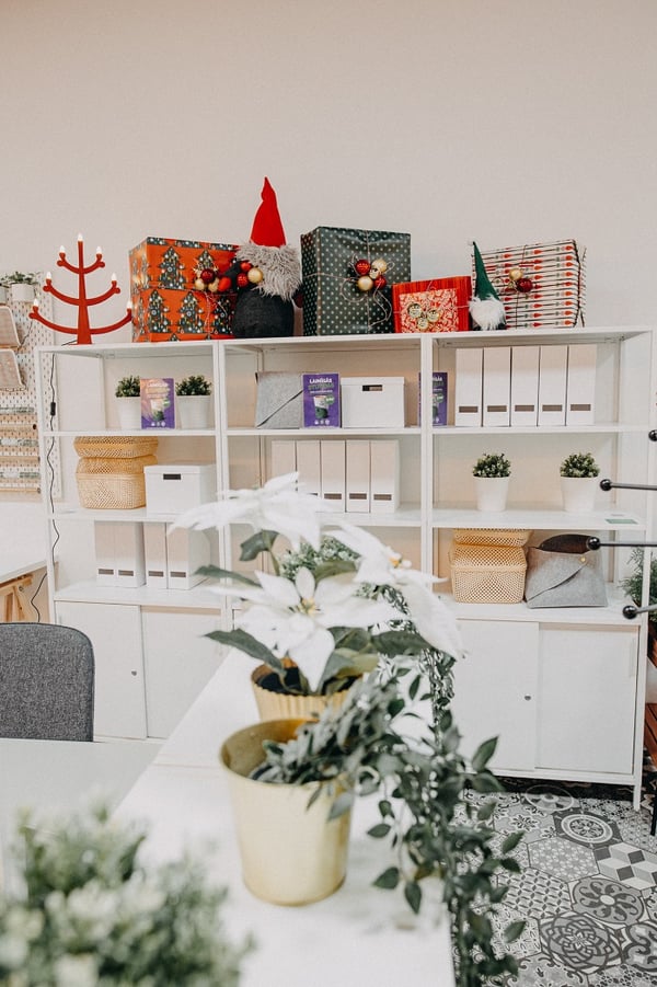 IKEA office storage area with white shelving units, holiday gift boxes, small plants, and decorative gnomes.