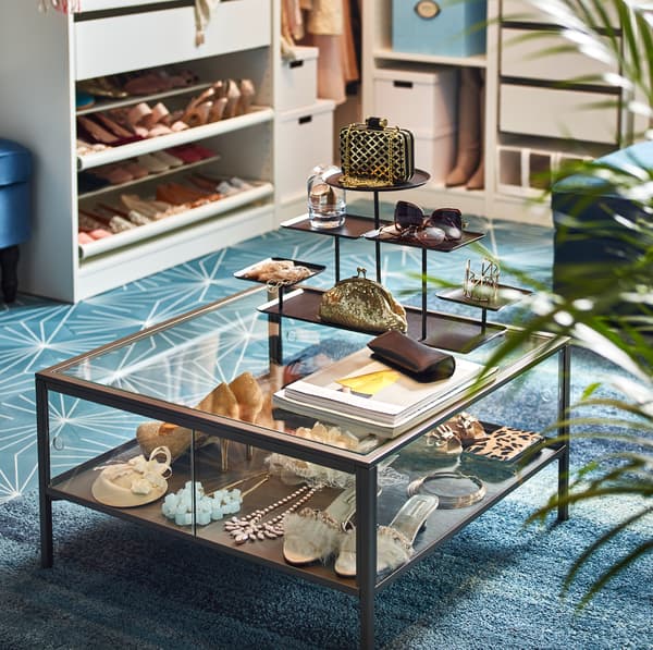 IKEA SAMMANHANG clear glass coffee table with black framed edges, showing purses and shoes.