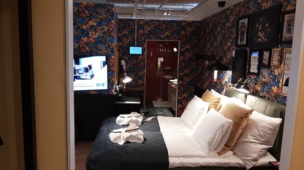 IKEA Schlafzimmer im Boutique-Hotel-Stil mit floral gemusterter Tapete, gemütlichem Doppelbett und eleganten goldenen Kissen – ideal für luxuriöse Einrichtungsideen aus dem IKEA Showroom.

